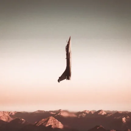 Jet aircraft climbing vertically above mountain peaks in a peach sunset sky