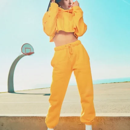 Woman in a yellow tracksuit and white boots beside a basketball hoop under a blue sky