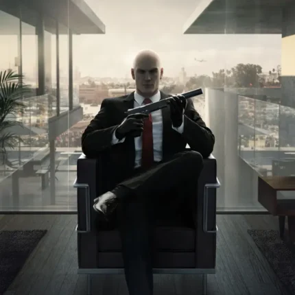 Bald man in a suit seated in an armchair holding a silenced pistol in a modern room