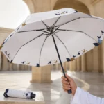 Cream folding umbrella with navy and gold crescent print held open in a courtyard