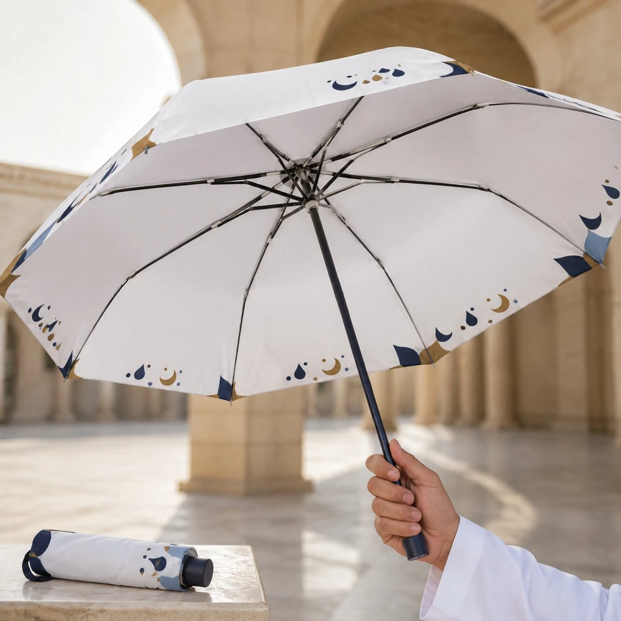 Custom Logo Hajj Umbrella with Crescent Moon Print Cream folding umbrella with navy and gold crescent print held open in a courtyard
