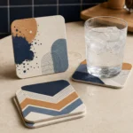 Square coasters with navy, mustard and arch line art under a glass of water