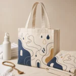 Cream cotton tote bag with navy and gold abstract print beside folded bags and prayer beads