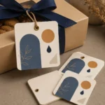 Square cream tags with blue arch and gold circle tied to a kraft gift box